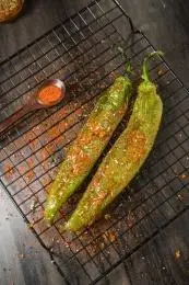 黑色烤架上放着两只撒着辣椒面的油炸青椒