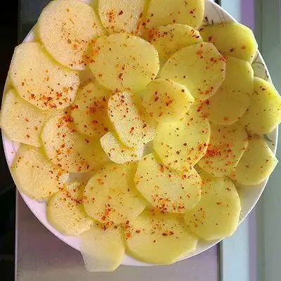 土豆切片,过水冲掉淀粉,加植物油和盐拌匀,摆盘,撒少许辣椒面,可加可