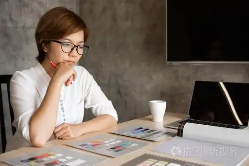 亚洲女设计师坐着思考. 有思想的建筑师女性牵着下巴,看着她的作品.