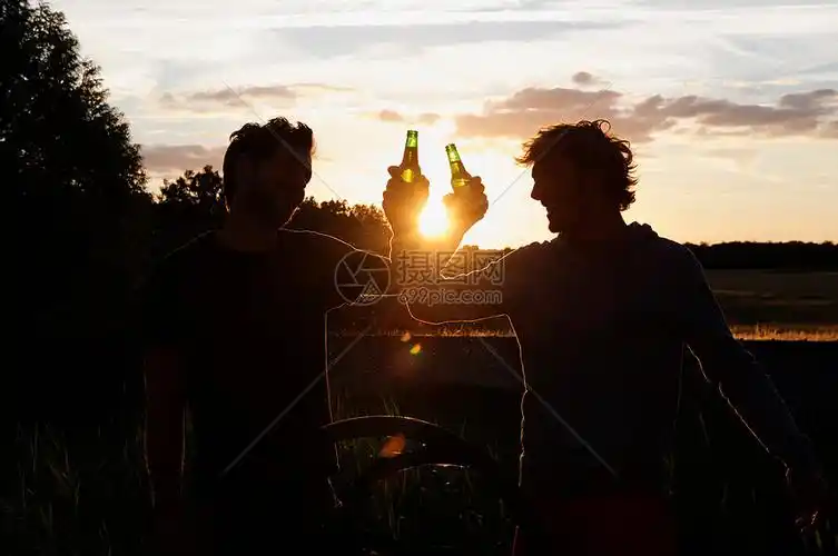 日落时喝啤酒的男人的剪影