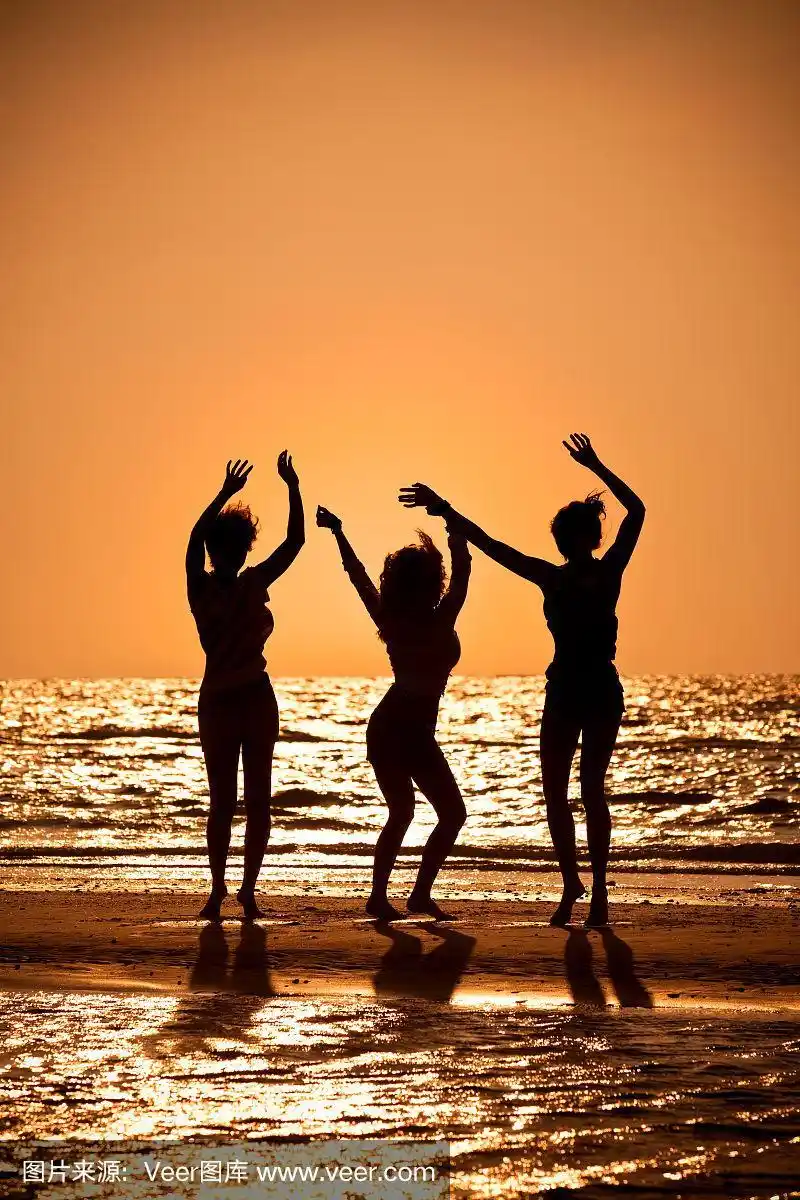 夕阳西下,三个穿着比基尼的美丽年轻女子在沙滩上翩翩起舞