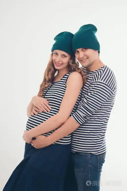 家庭肖像丈夫在白色背景上拥抱怀孕的妻子一男一女穿背心和帽子怀孕的