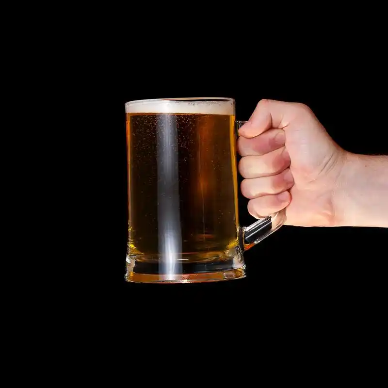 啤酒,黑色背景上拿着一杯啤酒的人的手.