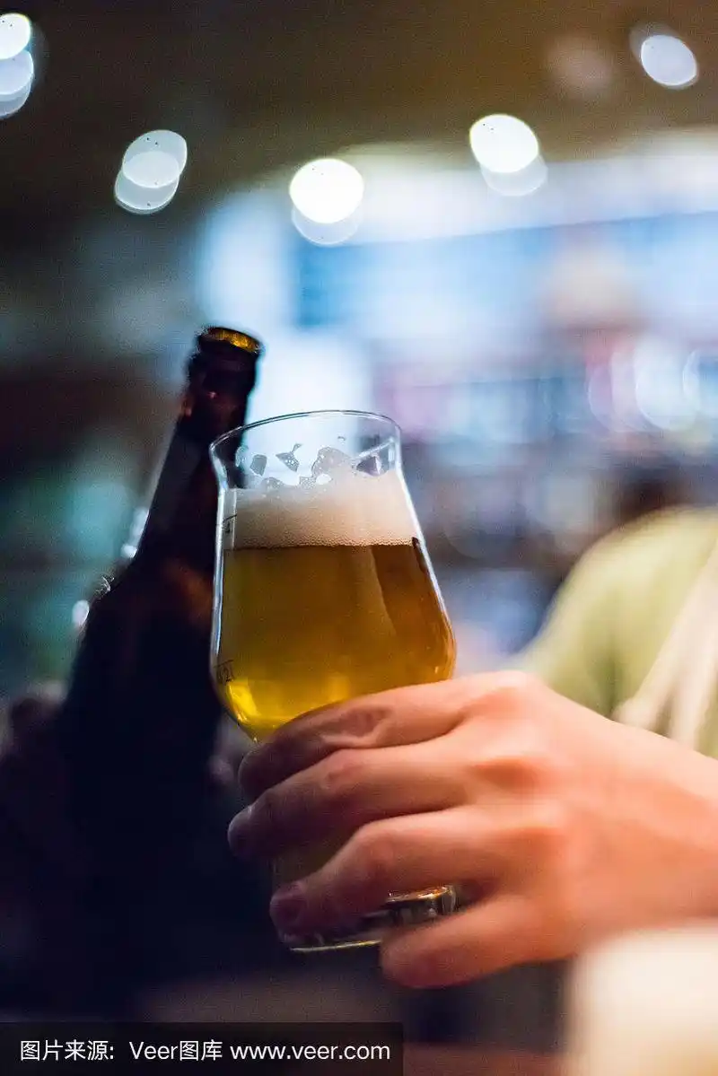 在酒吧里,男人的手拿着一瓶和一杯啤酒