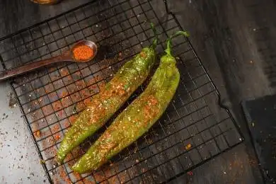 黑色烤架上放着两只撒着辣椒面的油炸青椒