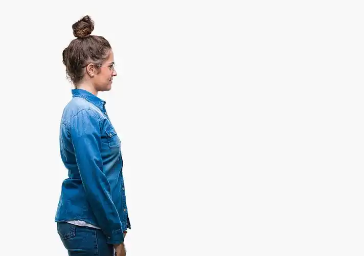 美丽的年轻的黑发卷发女孩戴眼镜在孤立的背景看向一边,放松的侧面