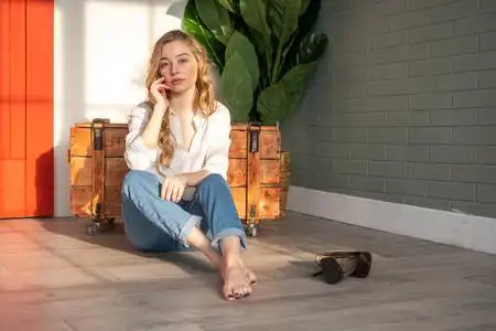 年轻漂亮的女人光着脚坐在木箱和绿色植物旁边的地板上照片