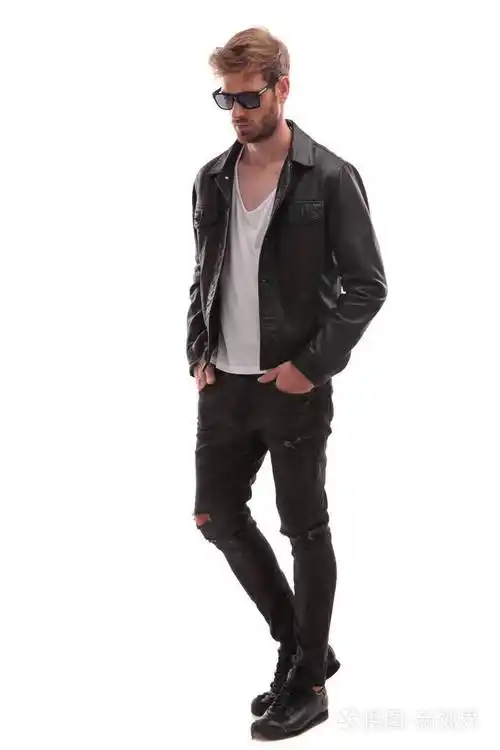 宽松的时尚男子与太阳镜和黑色皮革夹克走在白色的背景和看着侧面全身