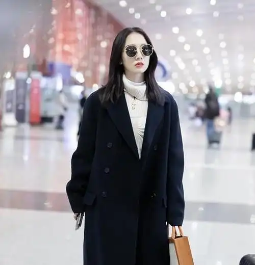 在纯白色的毛衣外面,孟美岐穿了一款深蓝色的长款风衣,深蓝色的衣服