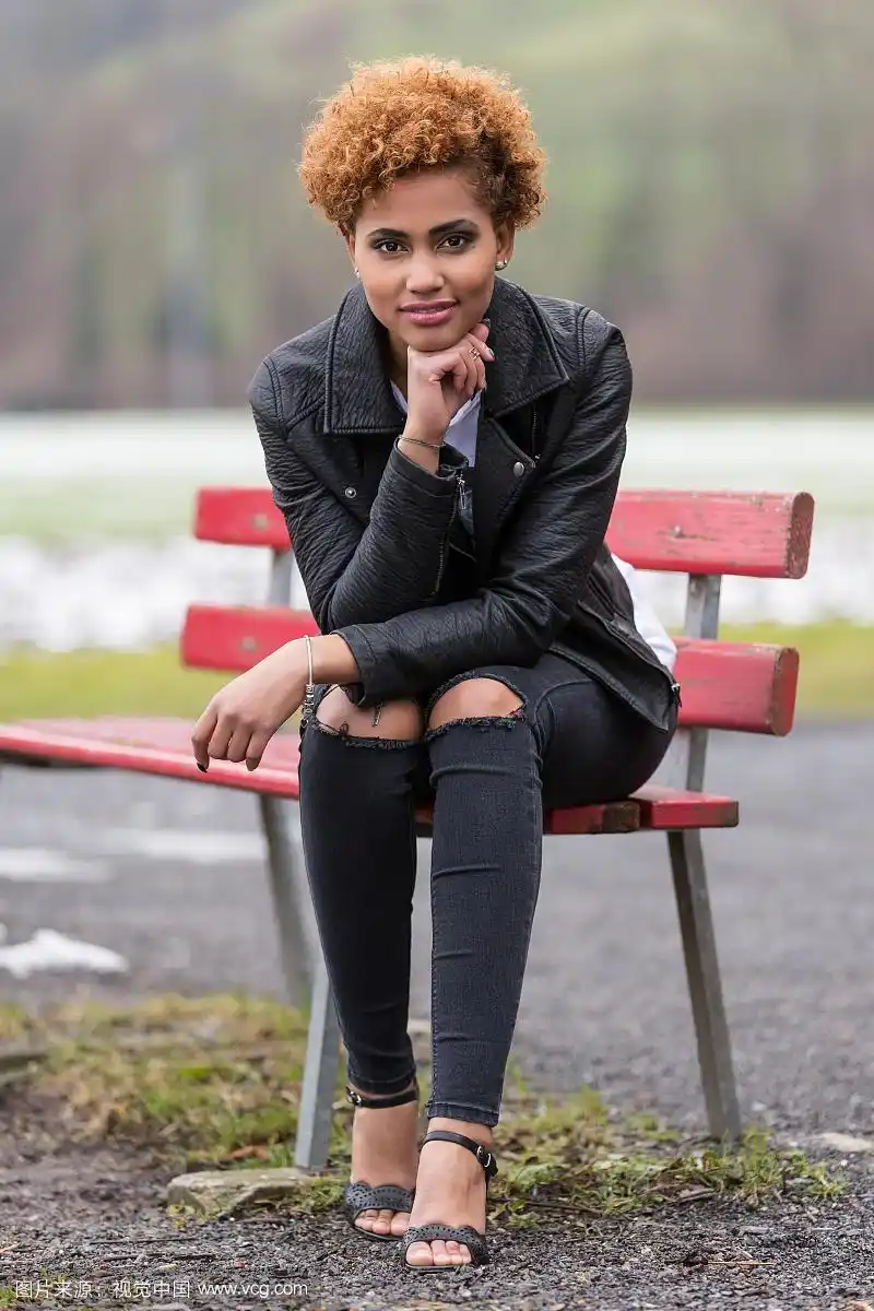 年轻的黑皮肤女人坐在长椅上,时尚