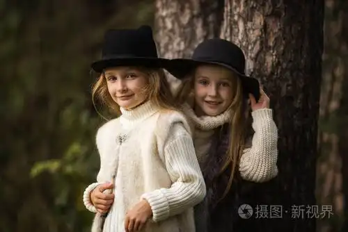 两个快乐的女孩同样穿着在森林的毛皮背心和帽子公园里的小女朋友儿童