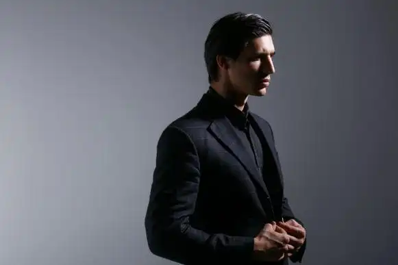 侧面肖像英俊的年轻人在黑色时尚的西装,孤立在灰色的背景.