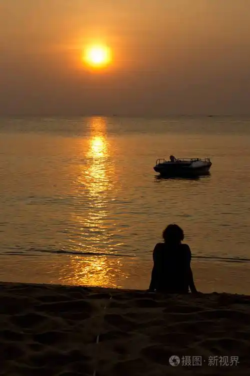 日落时坐在沙滩上的女人的剪影