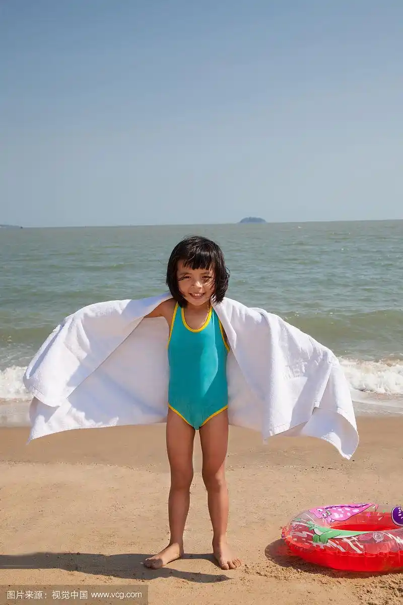 小女孩裹着浴巾站在沙滩上张开手臂