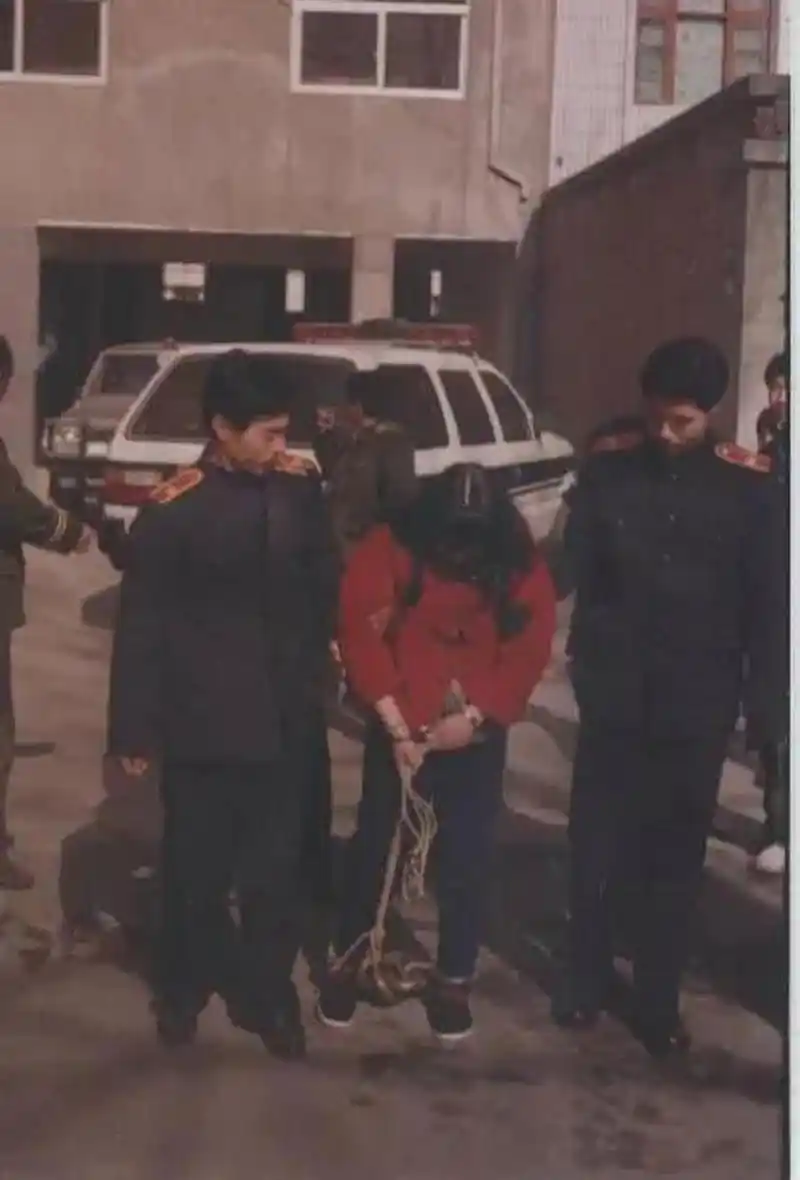 这是90年代,一名被押赴刑场的死刑犯,照片中的她穿着红色外套,脚上戴