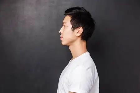 年轻亚洲男模的侧面肖像,穿着白色t恤,微笑着站着,看着身后黑色的工作