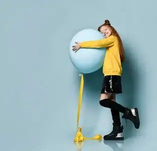 微笑着,拥抱着气球,在蓝色背景下侧身摆姿势.照片