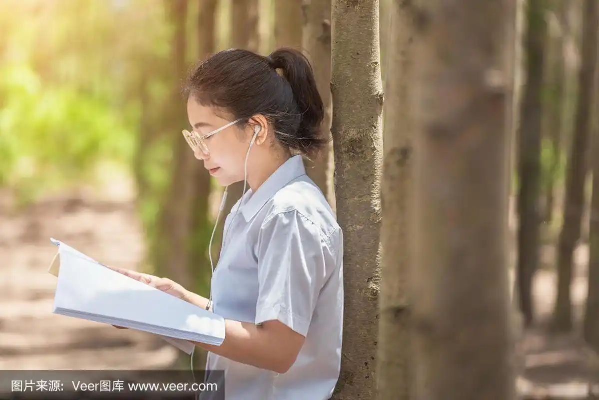 侧视图的高兴的深色头发的女人戴眼镜坐在长凳上和阅读的书在自然