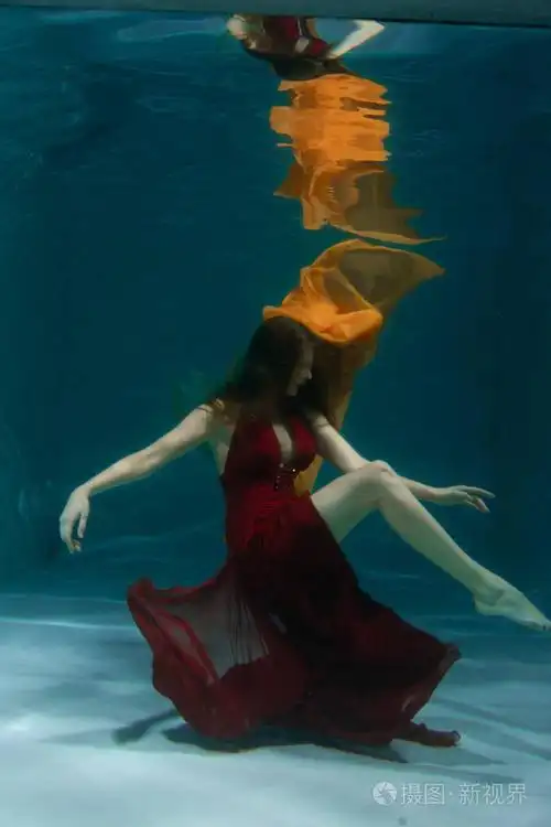 一个美丽的自由潜水员,一个人穿着红色的长裙,独自在深水中游泳