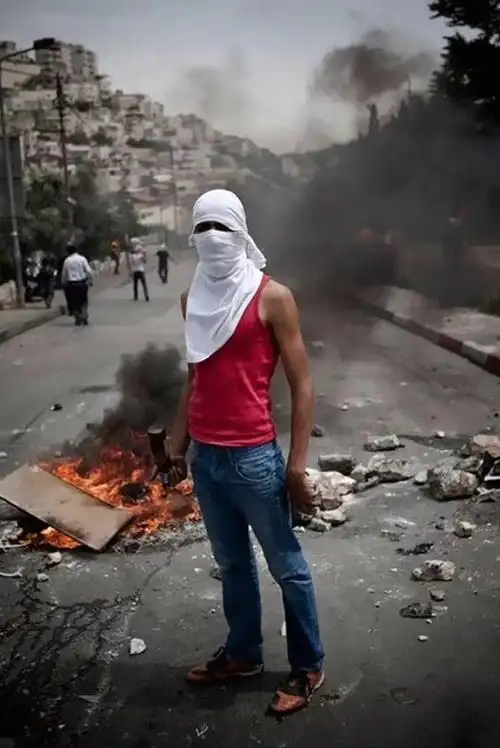 用白布蒙着头,后面是熊熊烈火,他手握石块,就像是一个可怕的"恐怖分子