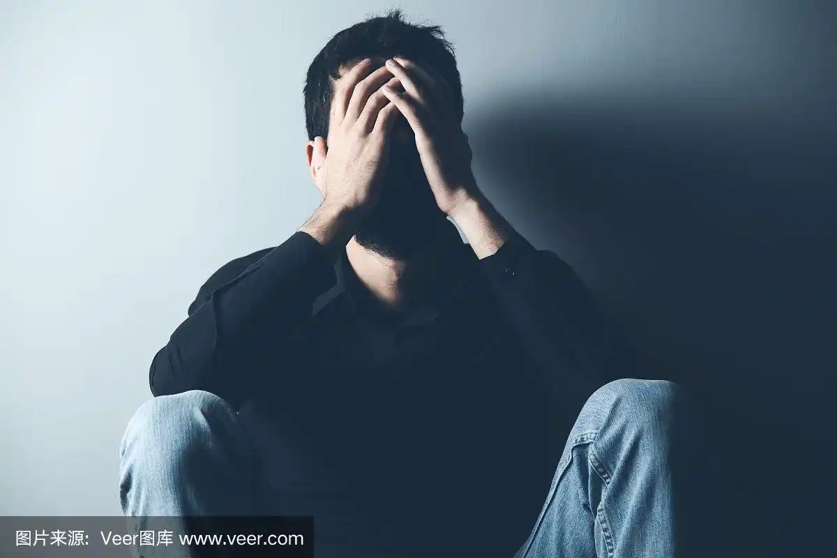 一个悲伤的男人坐在黑暗背景的地上