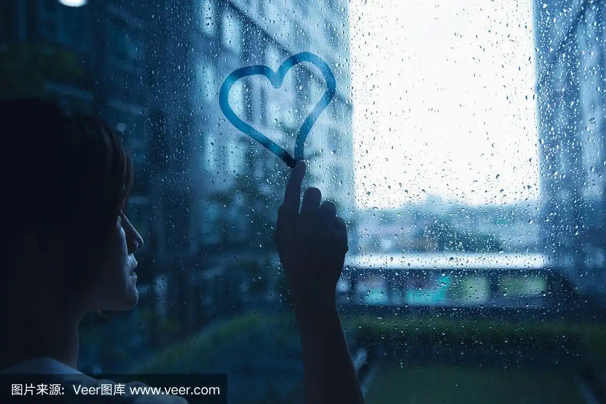 忧伤寂寞的爱女人在雨中把心画在窗户玻璃上深蓝色的色调