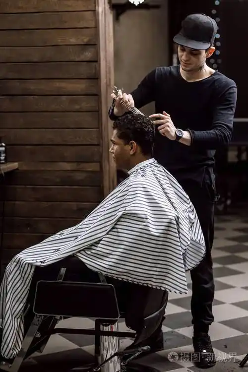 在一家理发店里一位穿着黑色衣服的理发师剪着坐在镜子对面的扶手椅上