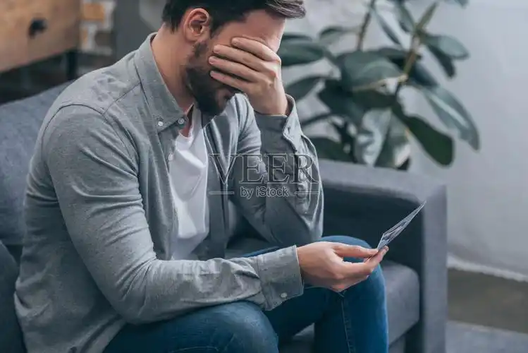 悲伤的男人坐在沙发上,拿着照片在家哭泣,悲伤的概念