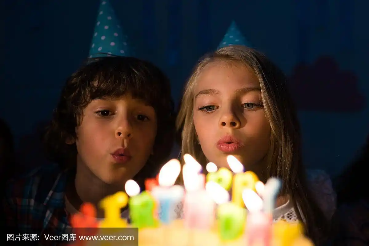 可爱的小朋友在派对帽上吹蜡烛在生日蛋糕上