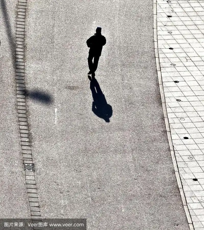 一个人走在街上,身后有一个长长的影子
