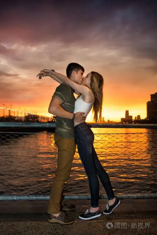 在日落的时候在市海洋码头附近的年轻美丽的夫妇在爱接吻