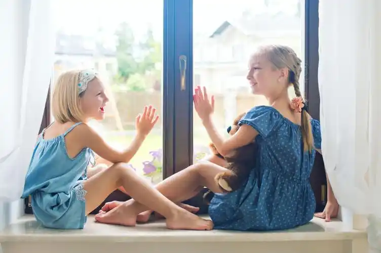 两个可爱的欧洲小女孩坐在靠近窗户的窗台上玩玩具