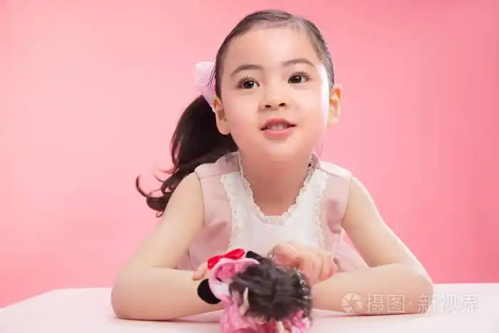 微笑可爱的小女孩在粉红色的背景下玩娃娃