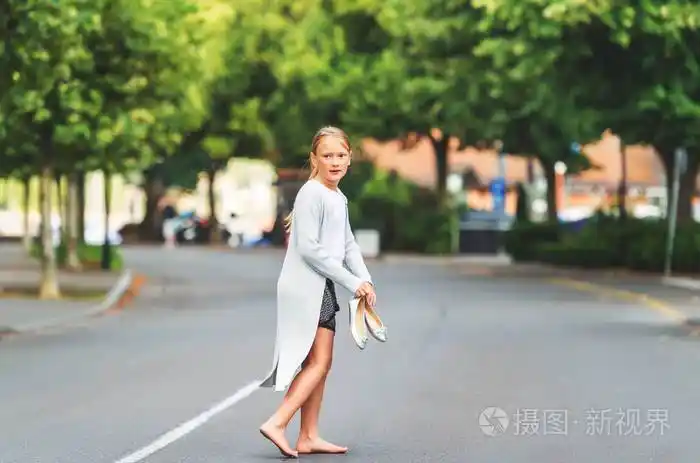赤脚小女孩走在街上戴着长灰色羊毛衫持有银弓芭蕾舞鞋