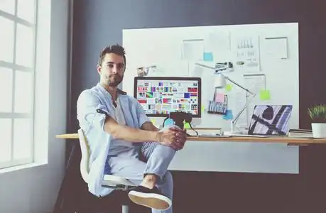 年轻设计师的肖像坐在平面工作室前的笔记本电脑和电脑, 而在线工作