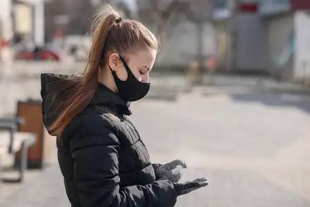 的女孩戴着防冠状病毒covid-19的健康面罩,在手术手套上喷洒消毒液