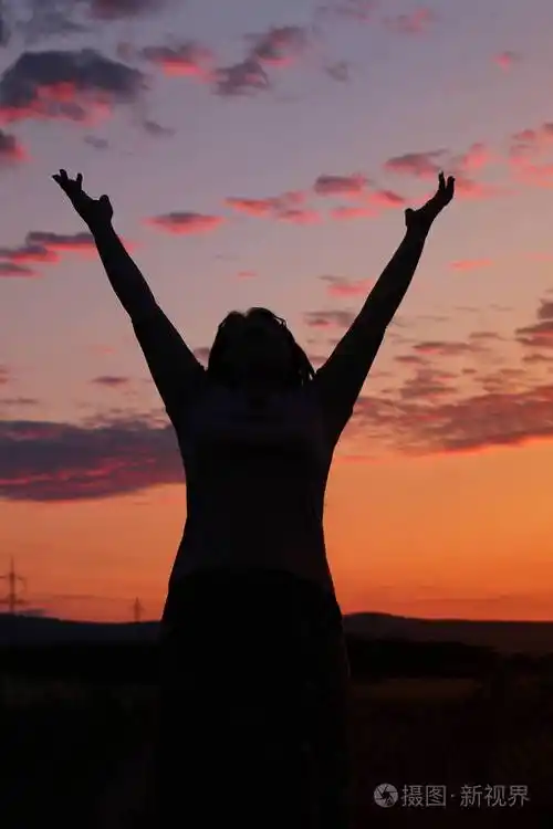 一个女人的黑影,她举起双手向天空举起,美丽的粉红色夕阳和紫色的云朵