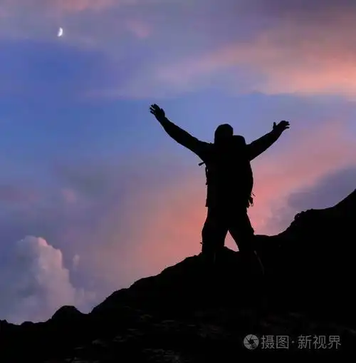 徒步旅行者的剪影,他们的手臂在日落的山顶上照片-正