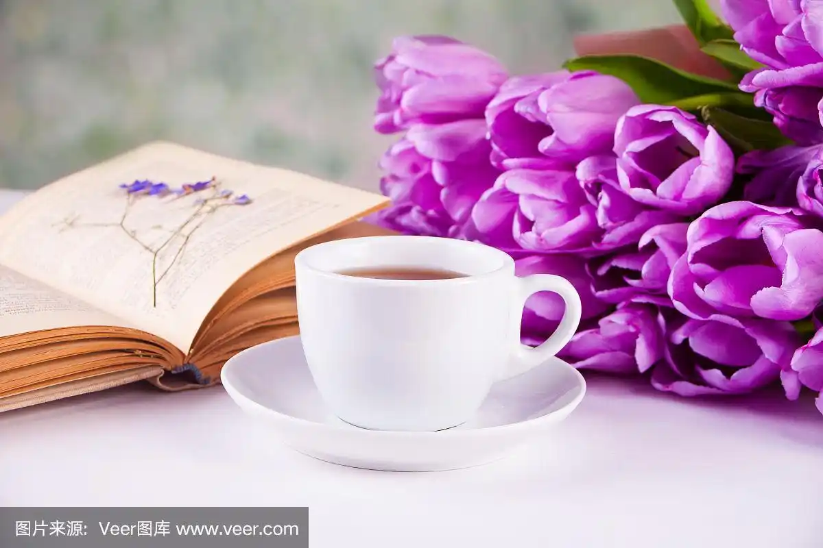 桌上放着一杯茶,一本书和紫罗兰花