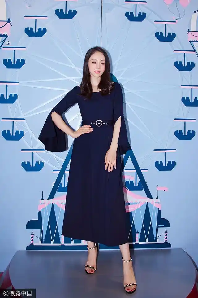 她身穿海军蓝开叉喇叭袖连身裙,脚踩珍珠镶嵌一字带高跟凉鞋.