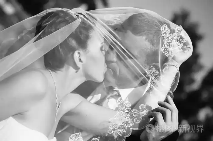 新娘和新郎在手拿鲜花花束的面纱下的亲吻照片-正版商用图片1j2ssa-摄