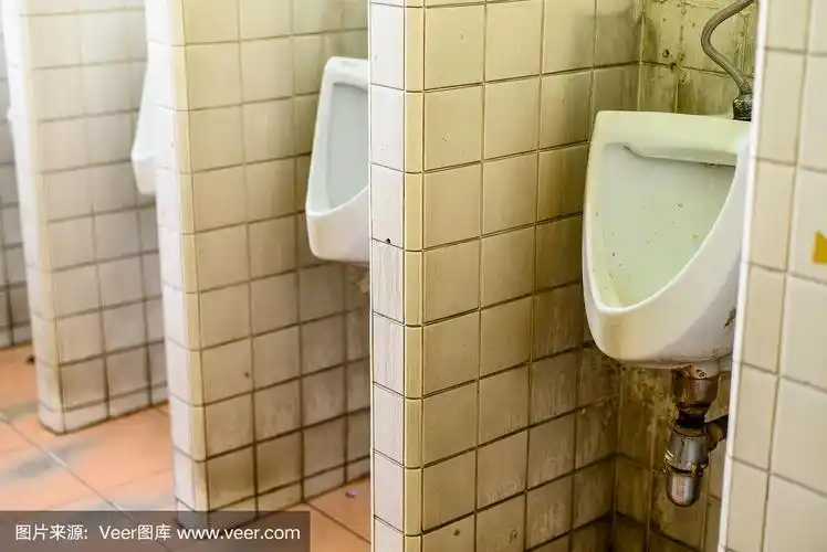 一排肮脏的小便池在公共厕所的瓷砖墙上