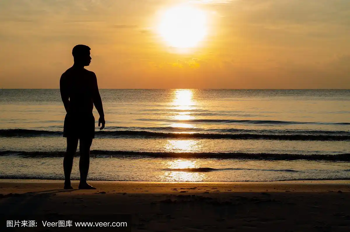 一个男人独自站在海滩上享受日出时刻的剪影照片