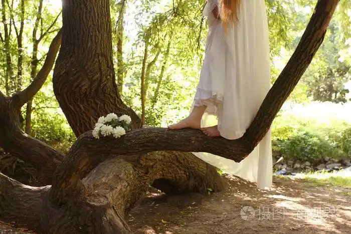 一个穿着白色长裙的女人赤脚在公园的树干上浪漫地散步