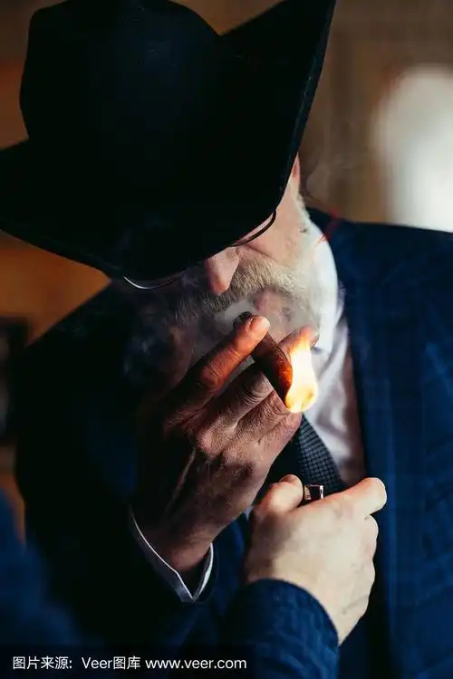 时髦的老人在宽边帽和丰富的蓝色西装吸烟