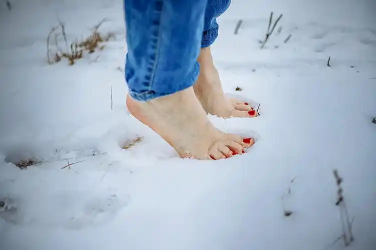 赤脚踩在雪地上:红色指甲与冷疗的概念.图片