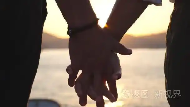 在日落时在海边的背景下男女手拉手的剪影年轻夫妇在户外拥抱爱和幸福