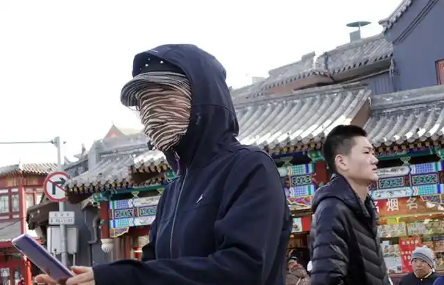 银锭桥上,一名游客用丝巾蒙住脸查看手机.