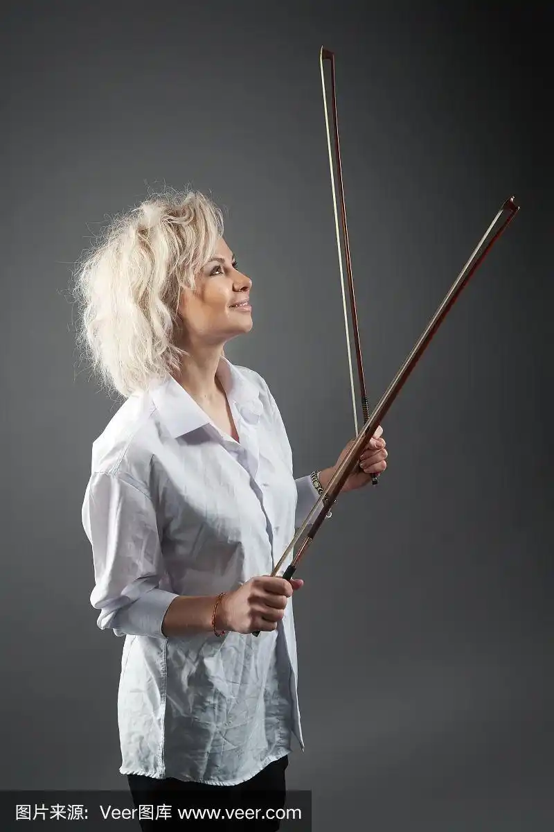 年轻的金发白人女孩小提琴手摆着两个小提琴弓