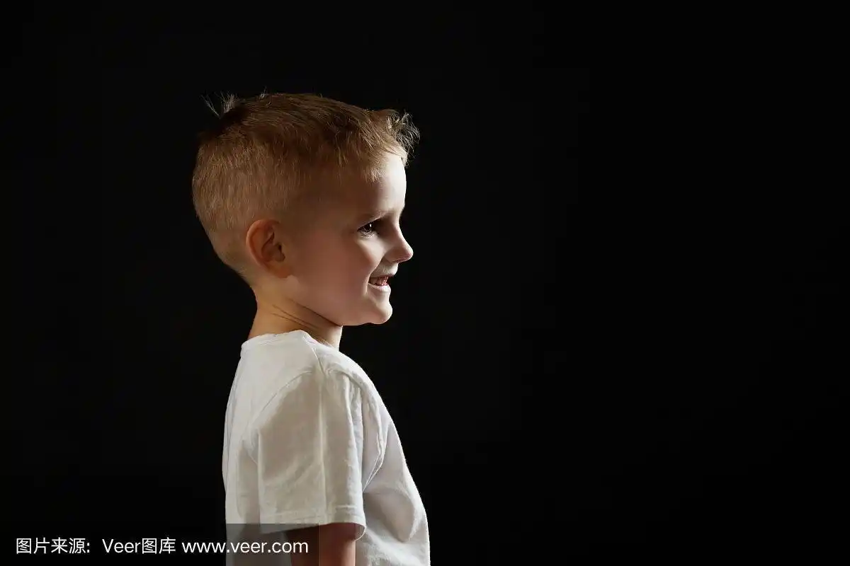 在黑色背景上的一个孩子的侧面肖像.男孩向前看,概念